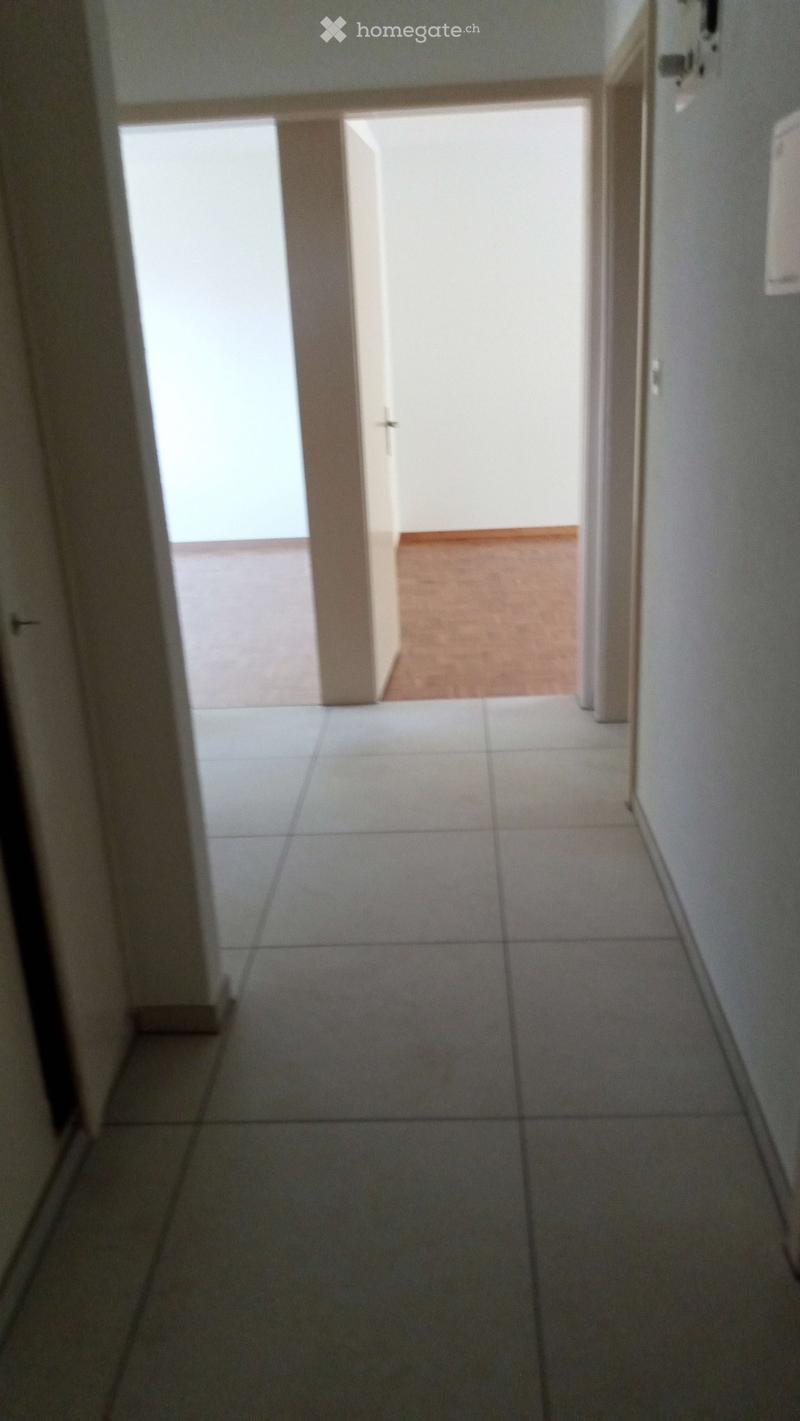 Empty hallway with tiled floor and white walls, leading to an open doorway with natural light.