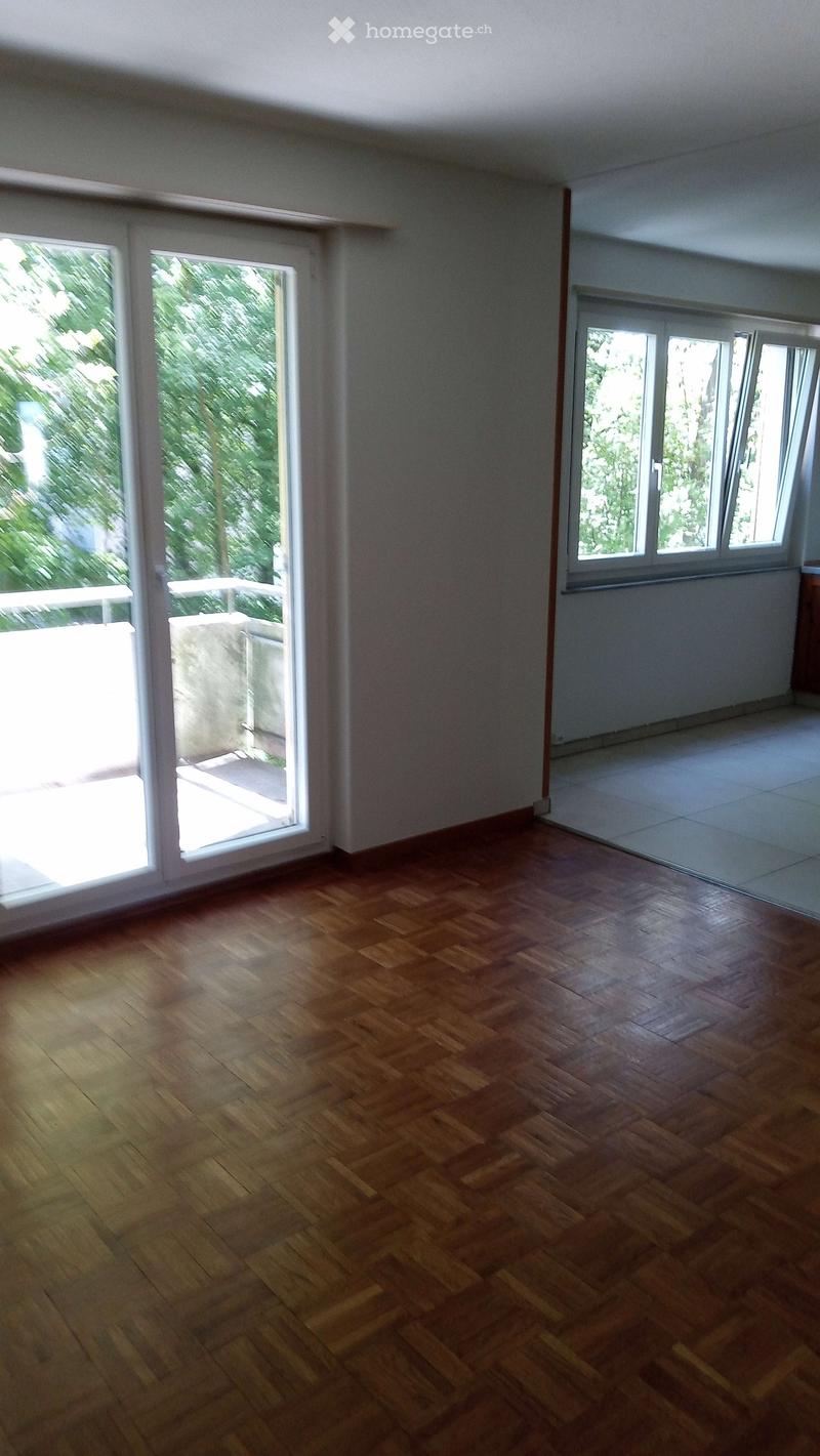 Empty room with wooden flooring, large windows, and sliding glass doors leading to a balcony.