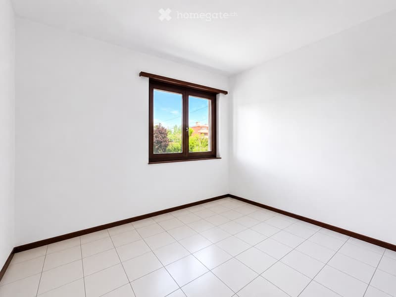 Empty room with white tiled floor and white walls, featuring a single window with wooden frame and sill.