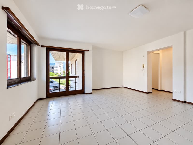 Empty room with white tiled flooring, white walls, large window, and sliding glass door leading to a balcony.