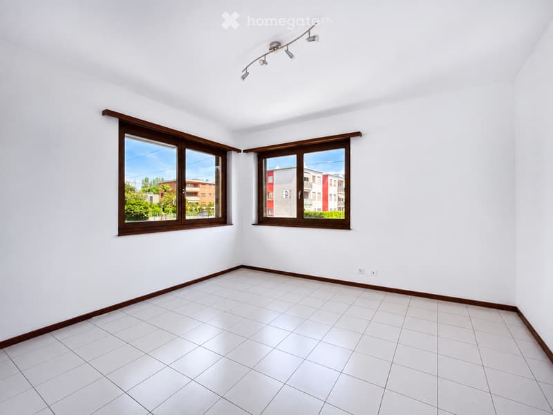 Empty room with white tiled floor, white walls, and large windows with wooden frames. Track lighting fixture mounted on the ceiling.