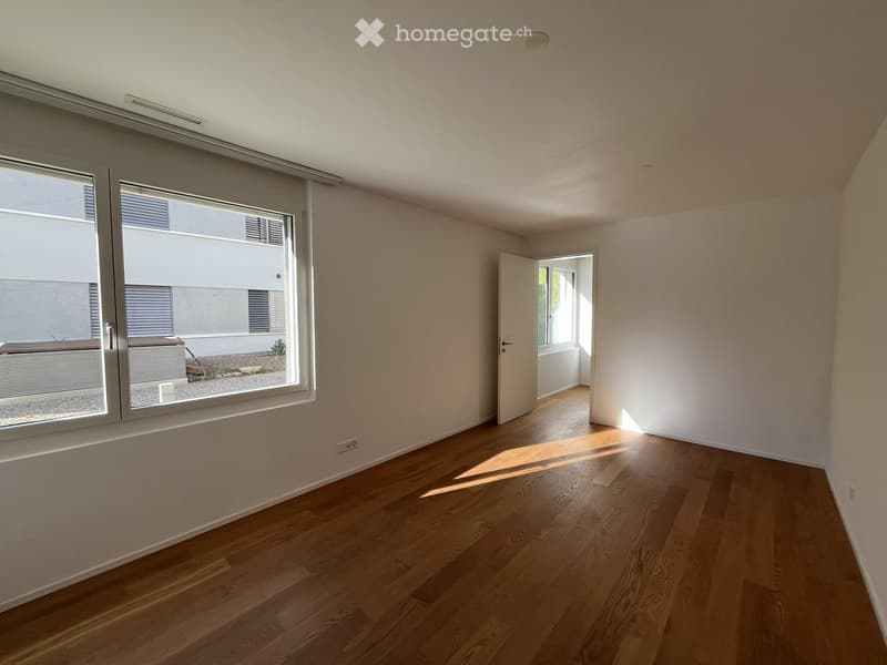Empty room with wooden flooring, large windows, and a door leading to another room.