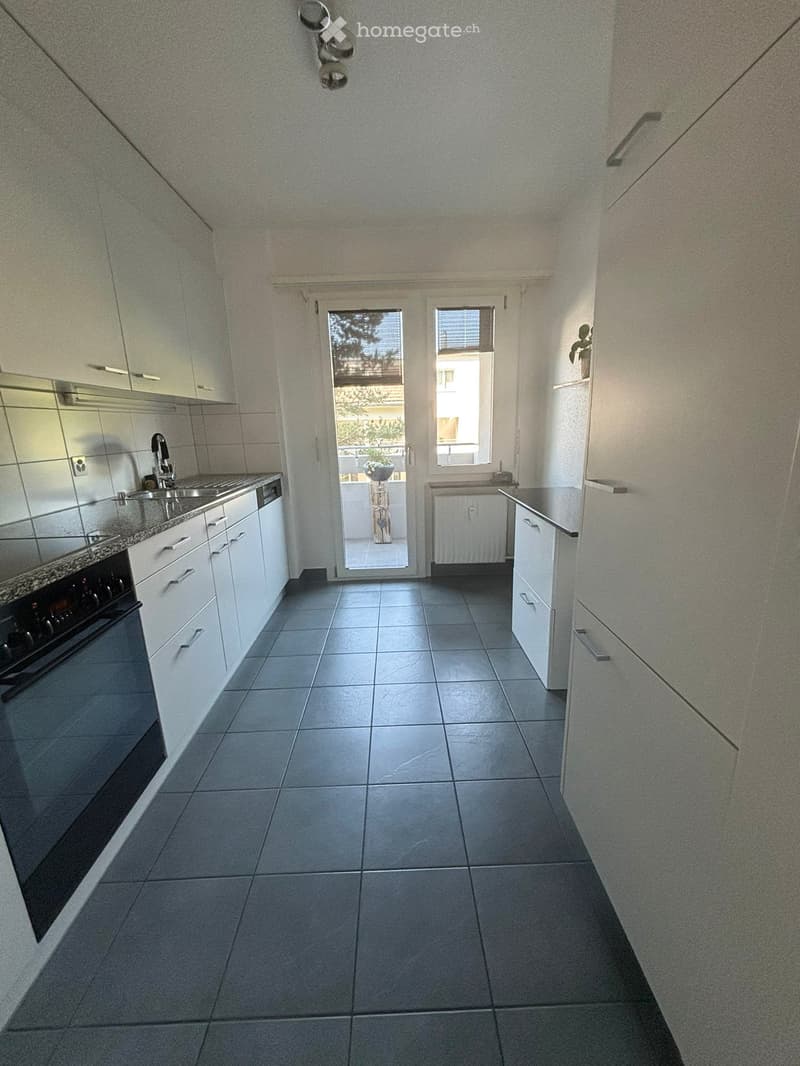 Modern kitchen with white cabinets, dark tiled floor, stainless steel oven, sink, and faucet. Features a sliding glass door leading to a balcony.