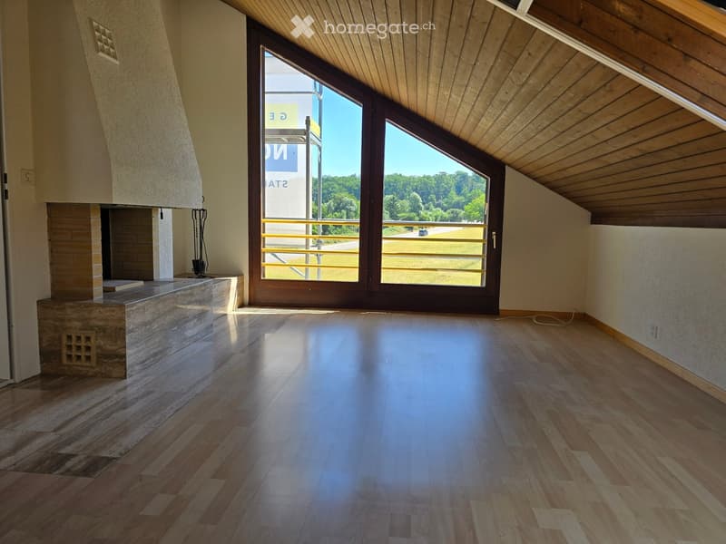 Empty room with wooden flooring, a fireplace, and large windows offering a view of the outdoors.