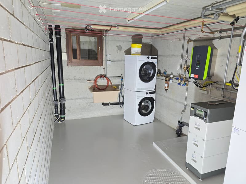 Utility room with a washing machine, sink, water heater, and electrical panel, exposed pipes and wiring.