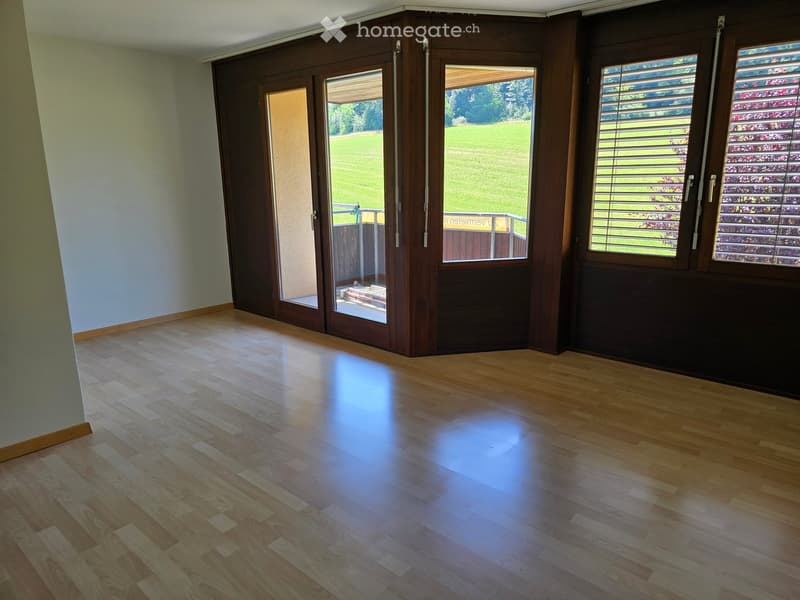 Empty room with wooden flooring, large sliding glass doors leading to a patio, and windows with blinds.