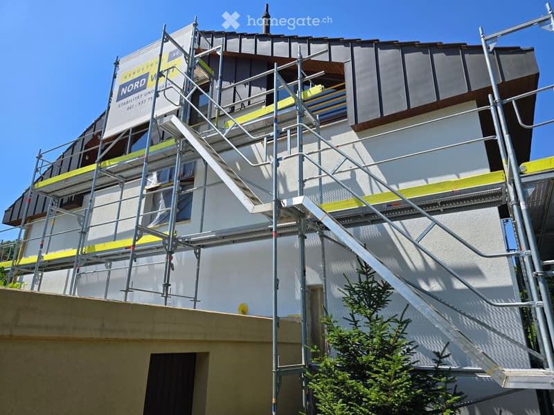 A multi-story building under construction with scaffolding, metal railings, and a partially covered roof.