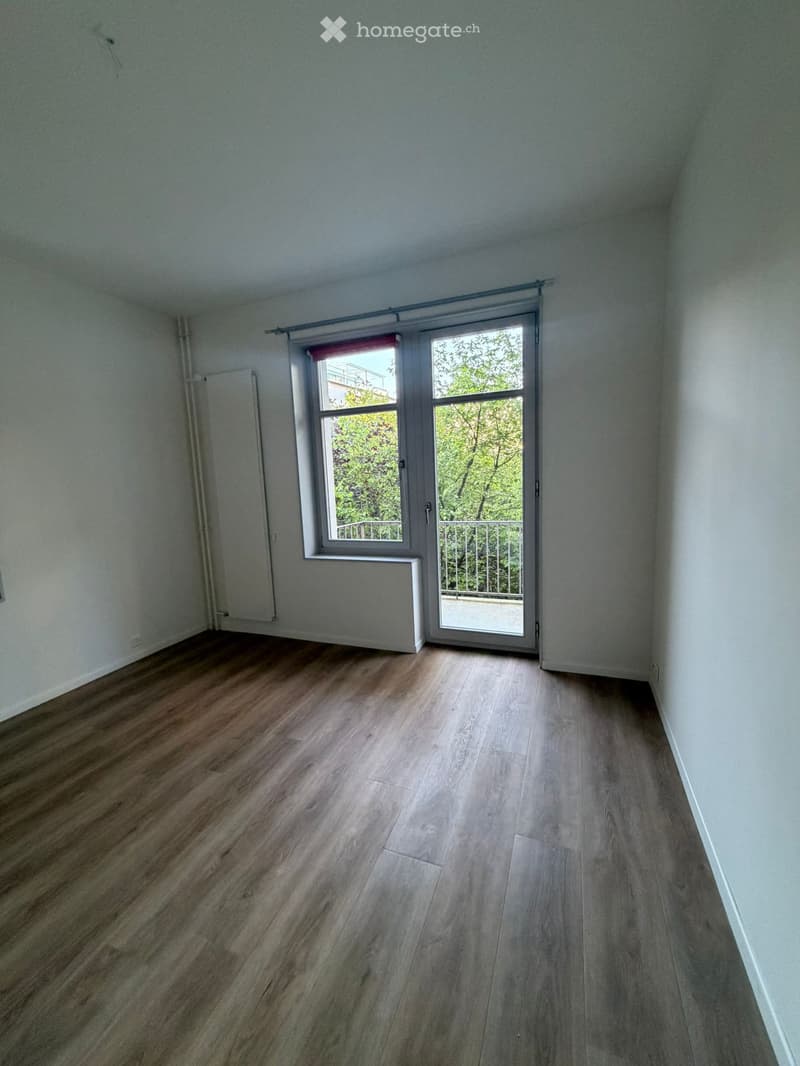 Empty room with light wooden flooring, white walls, and a large window with a sliding glass door leading to a balcony.
