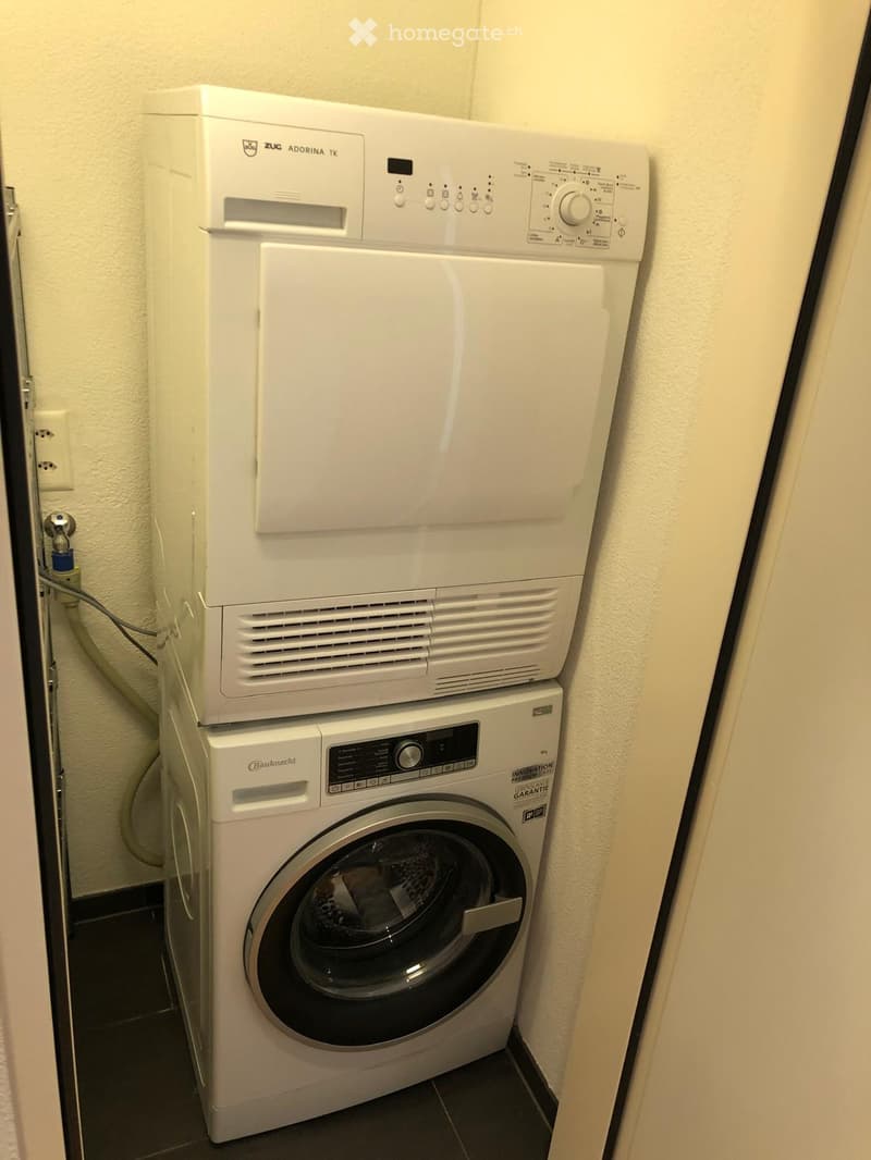 A compact bathroom with a white washing machine and a white dishwasher stacked vertically, featuring a control panel and a drum paddle.