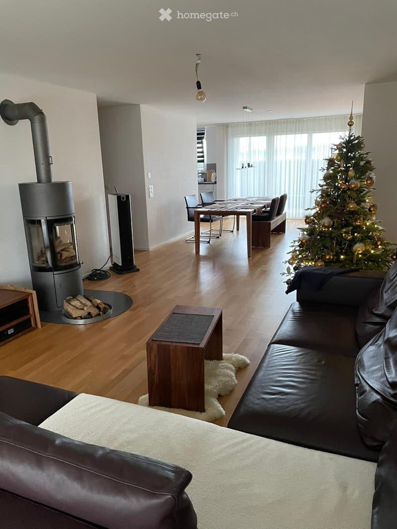 Modern living room with a black leather sofa, coffee table, fireplace, dining area with table and chairs, and a decorated Christmas tree.