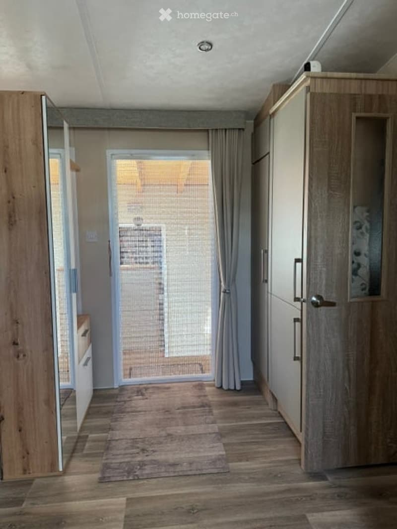 Modern hallway with wooden flooring, built-in wardrobe, sliding glass door leading to a balcony, and a small rug.