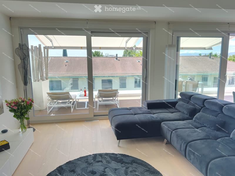 Modern living room with large glass doors leading to a balcony, grey sectional sofa, coffee table, and a small table with chairs on the balcony.