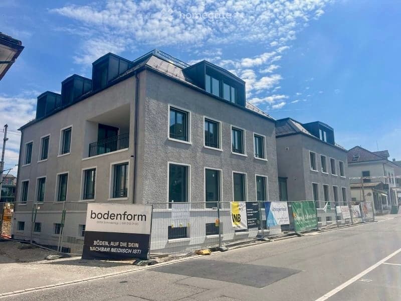 Building. Modern multi-story building with large windows and balconies, under construction with temporary fencing and signage.