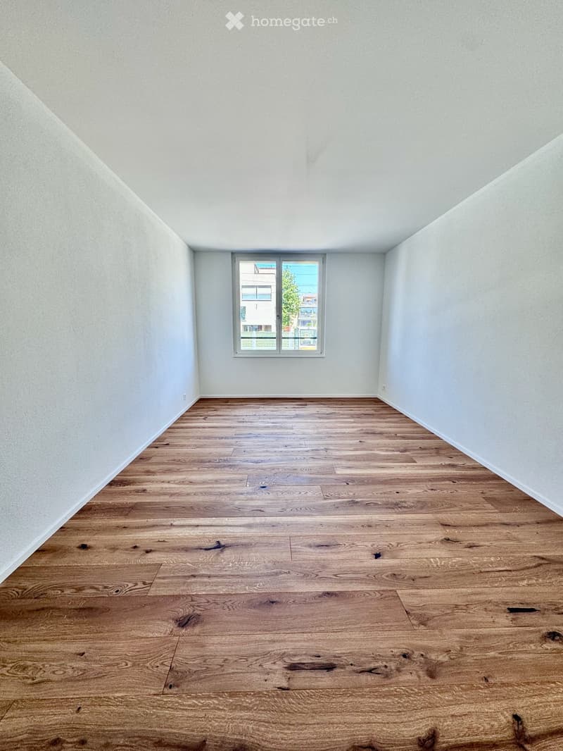Empty room with wooden flooring and white walls, featuring a single window with a view of the outside.