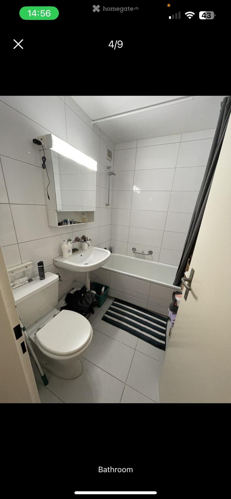 Modern bathroom with white tiles, a toilet, a sink, a bathtub, a mirror, and a small black and white rug on the floor.