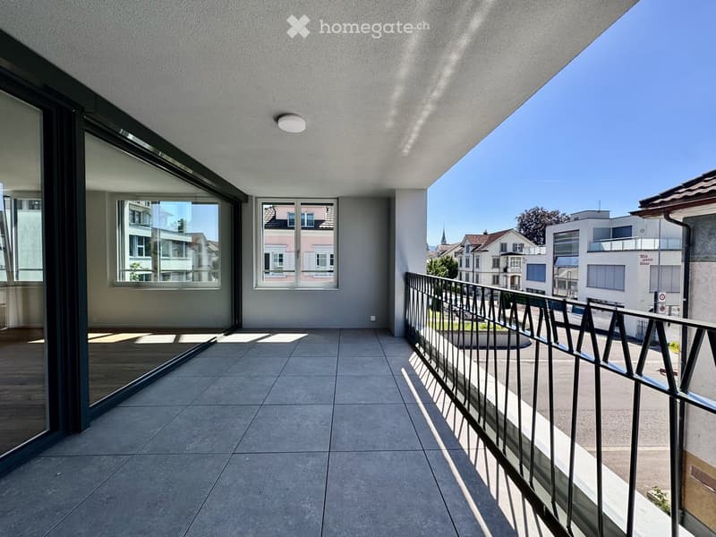 Modern balcony with tiled floor, glass railing, and large windows overlooking a cityscape.