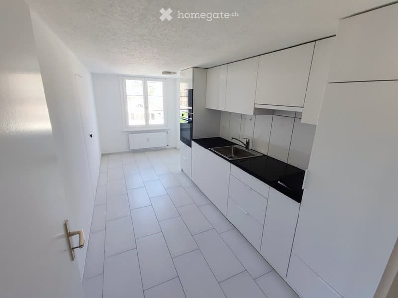 Modern, minimalist kitchen with white cabinets, black countertops, and white tiled flooring. Features a sink, faucet, oven, and radiator.