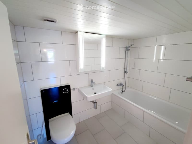Modern bathroom with white tiles, a toilet, a sink, a bathtub, and a mirror above the sink.