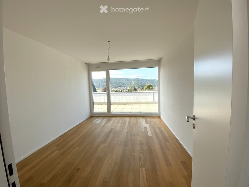 Empty room with wooden flooring, white walls, and a large window offering a scenic view of a landscape.