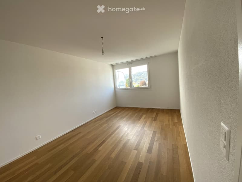 Empty room with wooden flooring, white walls, and a single window offering a view of the outdoors.