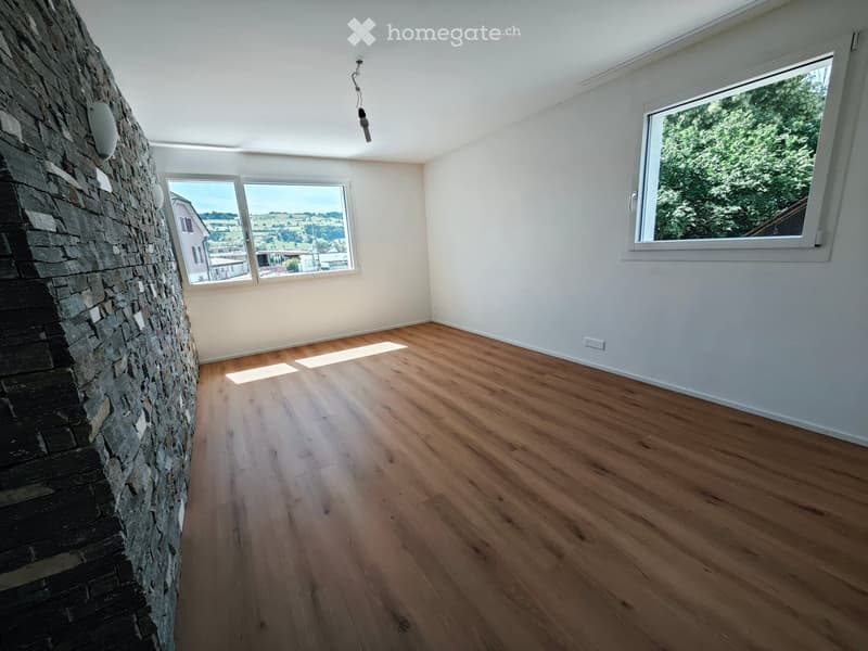 Empty room with wooden flooring, white walls, large windows, and a stone fireplace wall.