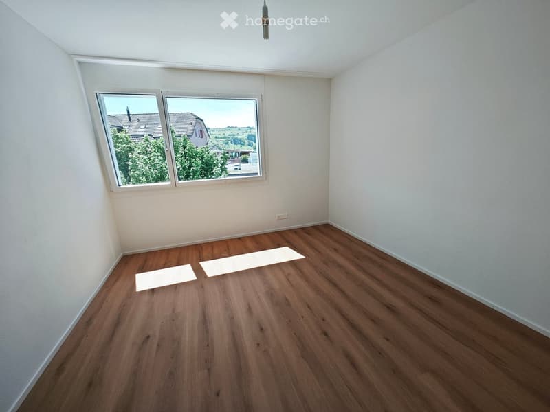 Empty room with wooden flooring, white walls, and large windows offering a view of the outside. No furniture or equipment present.