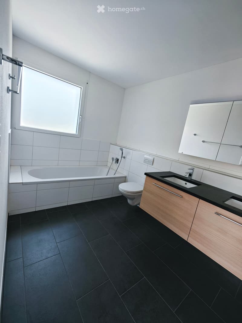 Modern bathroom with black tiled floor, white tiled walls, bathtub, toilet, sink, and mirrored cabinet.