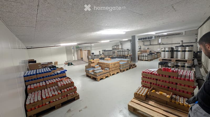 Warehouse with rows of stacked pallets containing cans and barrels, organized storage area with industrial lighting and concrete floors.