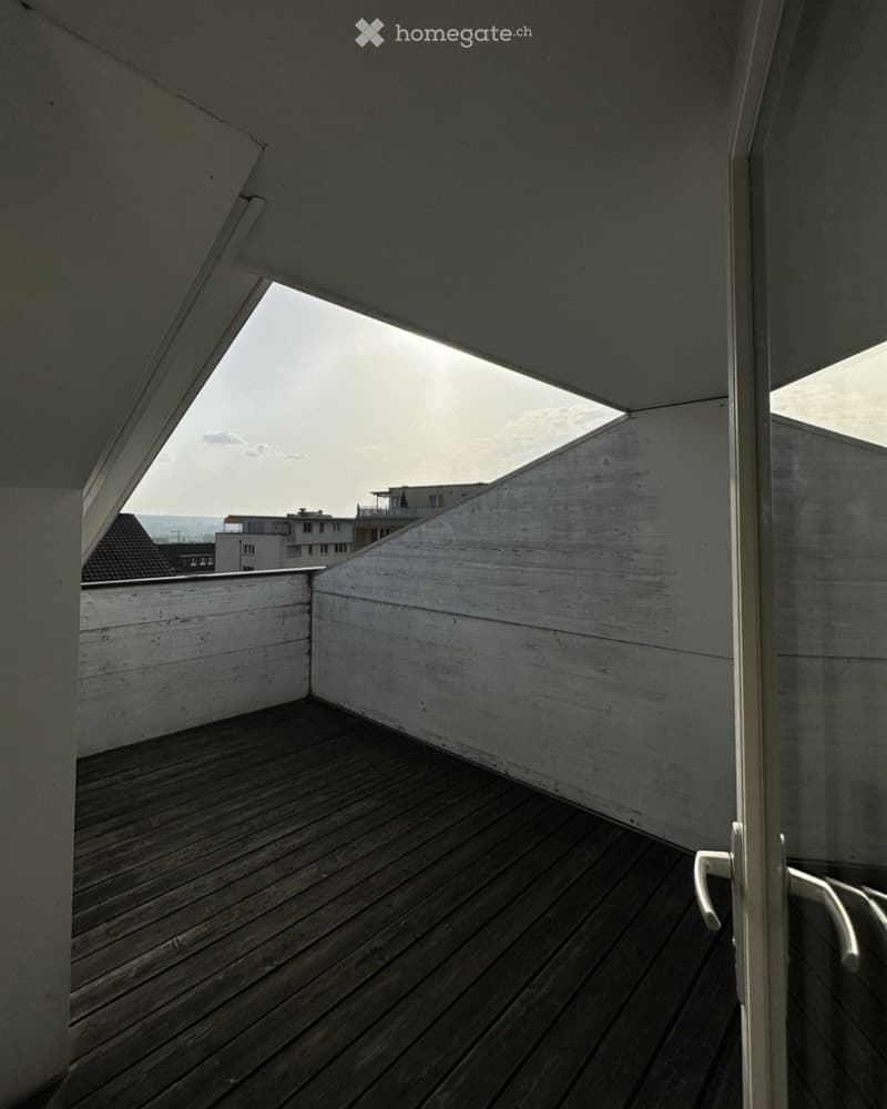 Modern wooden balcony with white concrete walls and a glass door leading inside, offering a view of the cityscape.