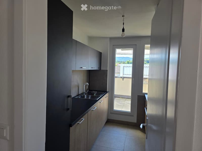 Modern kitchen with sleek cabinets, a black countertop, and a stainless steel sink. A large window offers a view of the outdoor area.