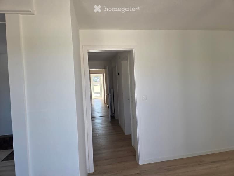 Empty hallway with white walls, wooden flooring, and multiple doors leading to other rooms.