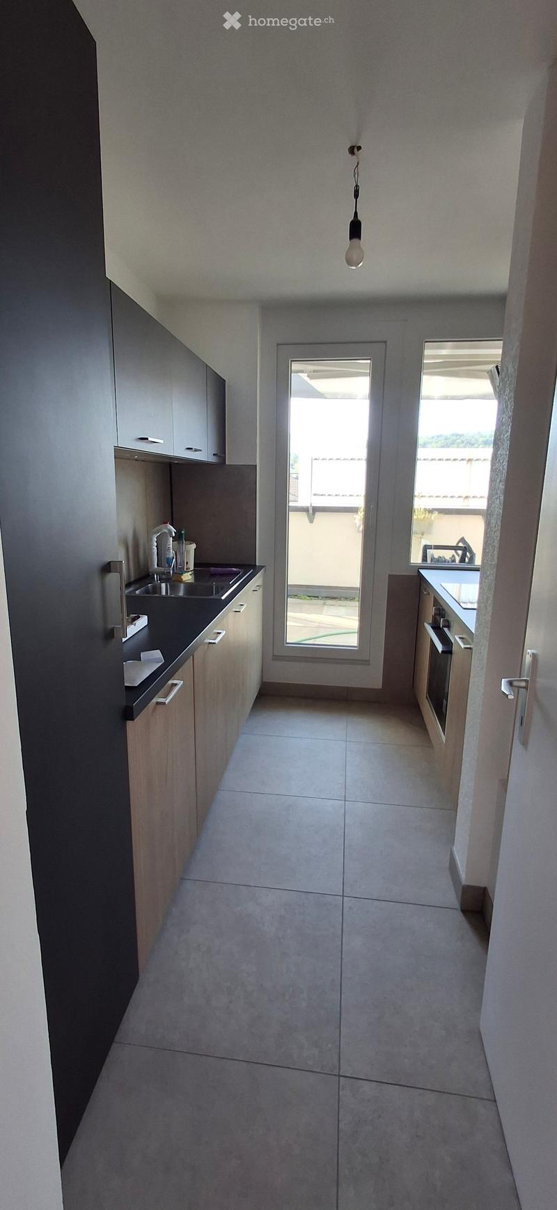 Modern kitchen with light wood cabinets, black countertops, and a large window overlooking a balcony area.