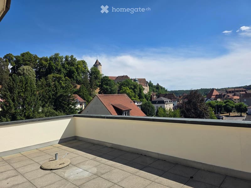 Flat rooftop terrace with tiled surface, low parapet wall, and scenic view of town and castle.