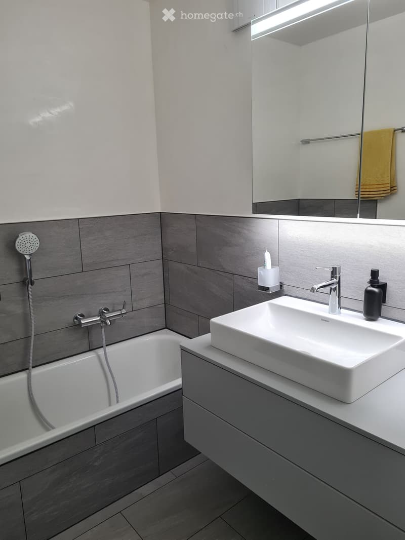 Modern bathroom with a white sink, bathtub, mirror, and a towel hanging on the side.