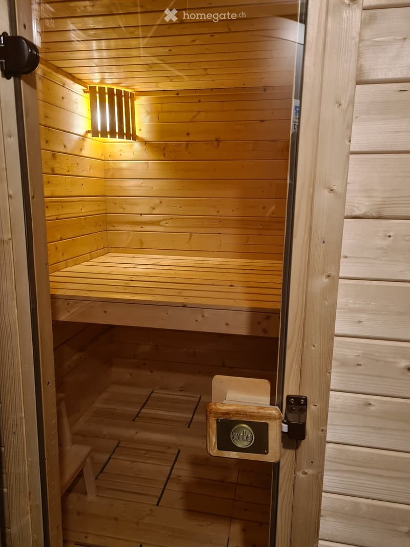 Wooden sauna interior with built-in benches and a small light fixture on the wall.