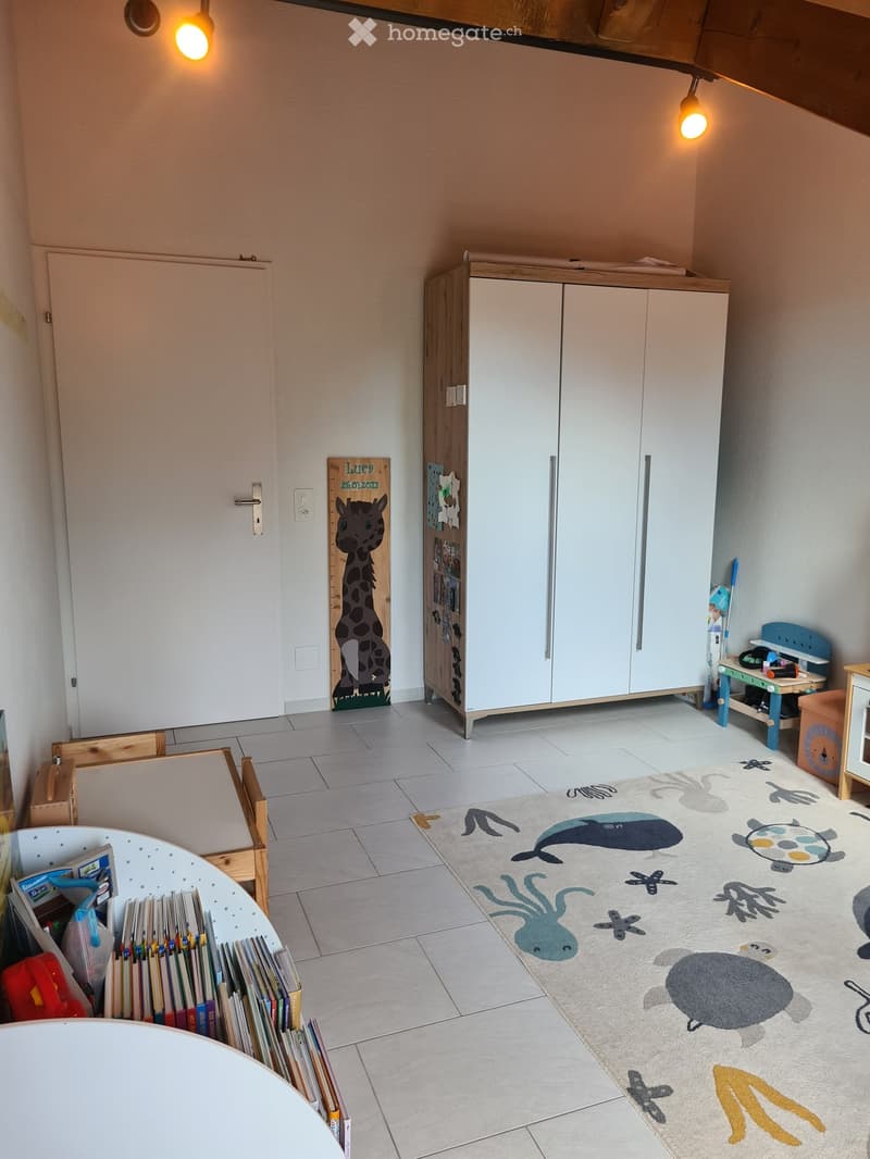 Child's room with a large white cabinet, bookshelf, small table, chair, and a rug with sea animal designs.