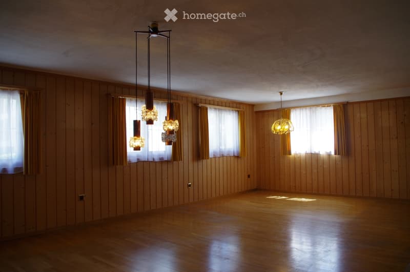 Completely empty room with wooden walls and floor, large windows with curtains, and modern pendant lights.