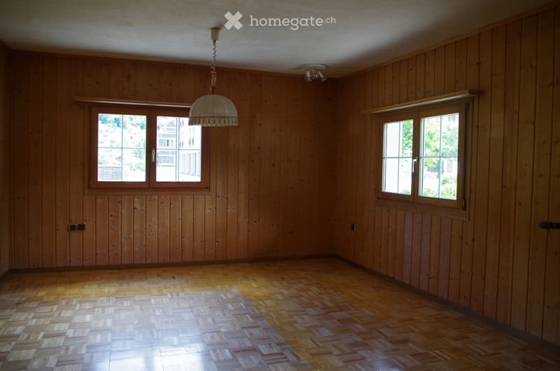 Empty room with wooden walls and floor, two windows, and a hanging light fixture.
