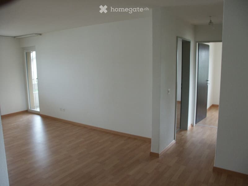 Empty room, hardwood floors, white walls, two doors, sliding door leading to balcony, no furniture