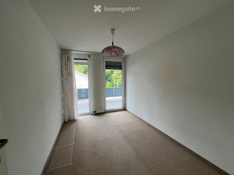 Empty room with light-colored walls, carpeted floor, and a ceiling light fixture. Features a large sliding glass door leading to a balcony or outdoor area.
