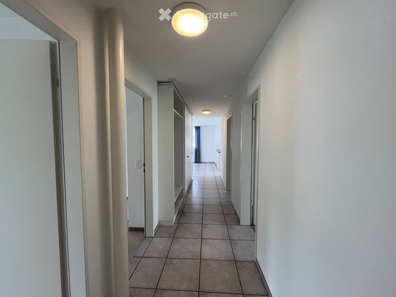 Empty hallway with tiled floor, white walls, and several doors leading to rooms.