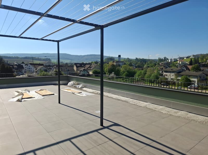Roof terrace with tiled floor, metal frame, and a view of a town and surrounding landscape.