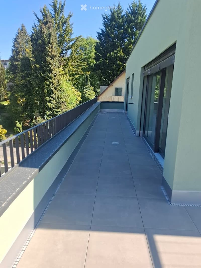 Modern balcony with tiled flooring, metal railing, and a view of tall trees and neighboring building.