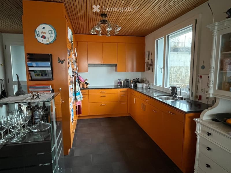 open kitchen with orange cupboards, granite countertops, central island with sink, large chandelier, wine glasses, bottles, drawers, tiled floor