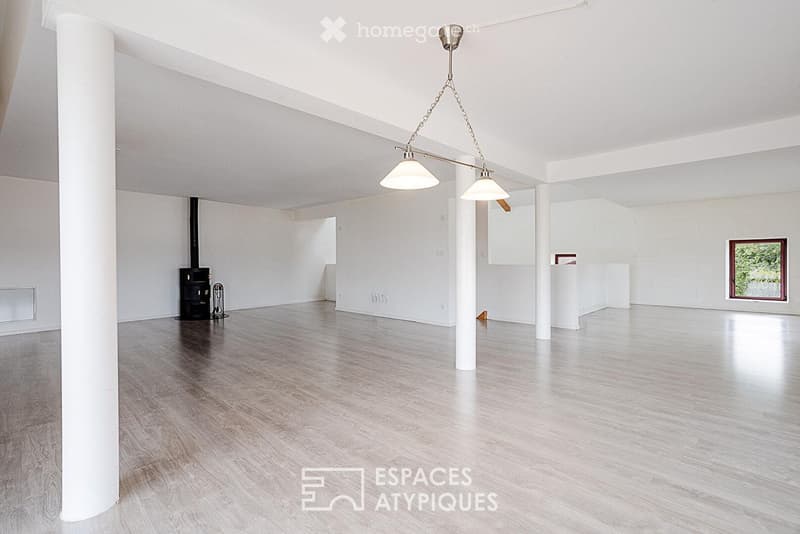 Empty room with white walls, wooden floor, white columns, and a hanging light fixture. A small black stove is visible in the corner.