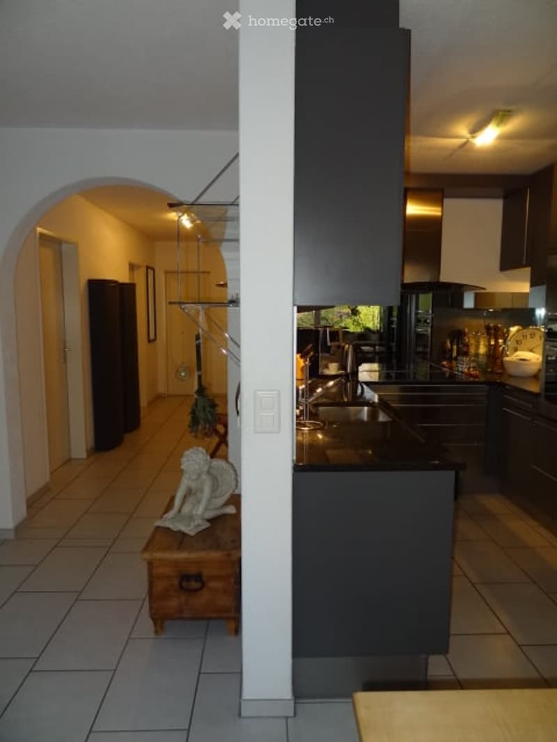 Modern kitchen with dark cabinets, a central island, and a sink. A small table with a statue sits in the adjacent hallway.