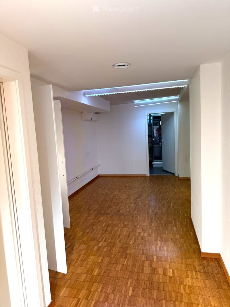 Corridor / Hallway. Empty hallway with wooden flooring, white walls, and recessed lighting. Features an open doorway leading to another room.