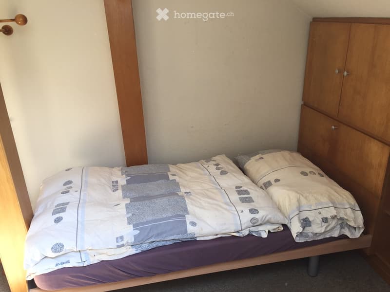 small bed, two pillows, purple blanket, wooden cabinet with shelves