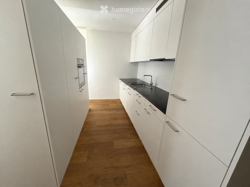 Modern kitchen with white cabinets, black countertop, wooden floor, and stainless steel sink and oven.