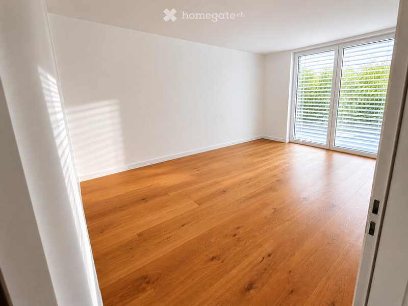 Empty room with light wooden flooring and white walls, featuring a large sliding glass door with blinds leading outside.